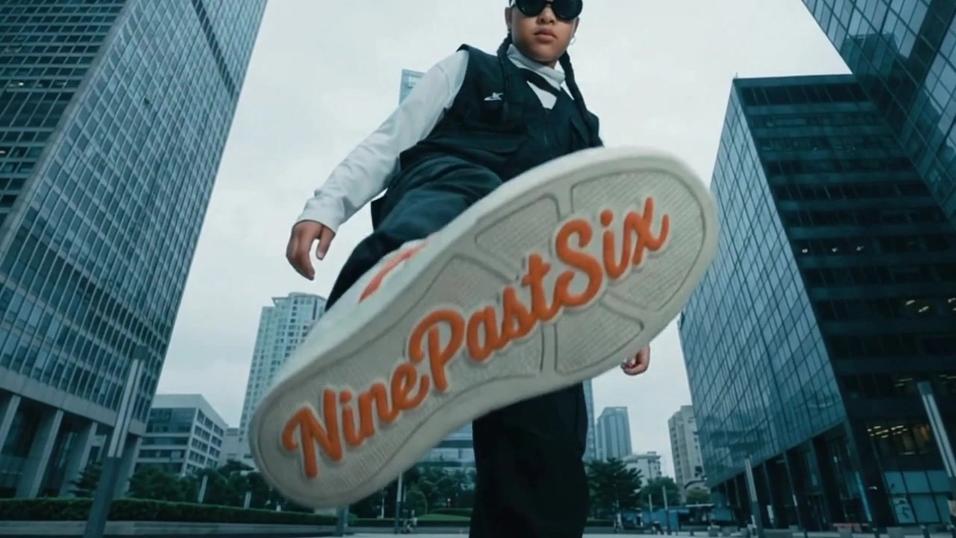 NinePastSix campaign still with a branded sneaker sole framed between city buildings.